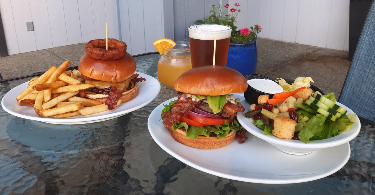 Two Cafe 95 burgers with fries and a fresh salad on the patio